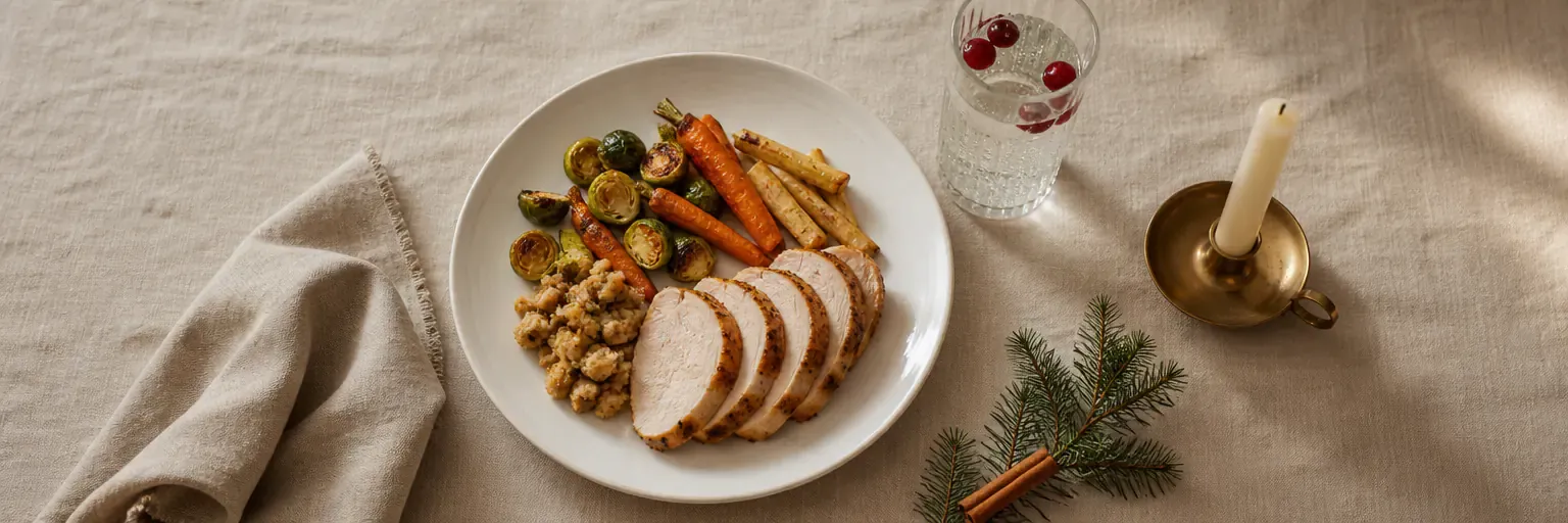 Overhead view of a single measured Thanksgiving dinner plate with roast turkey, roasted vegetables, and stuffing beside a glass of sparkling water on a linen tablecloth