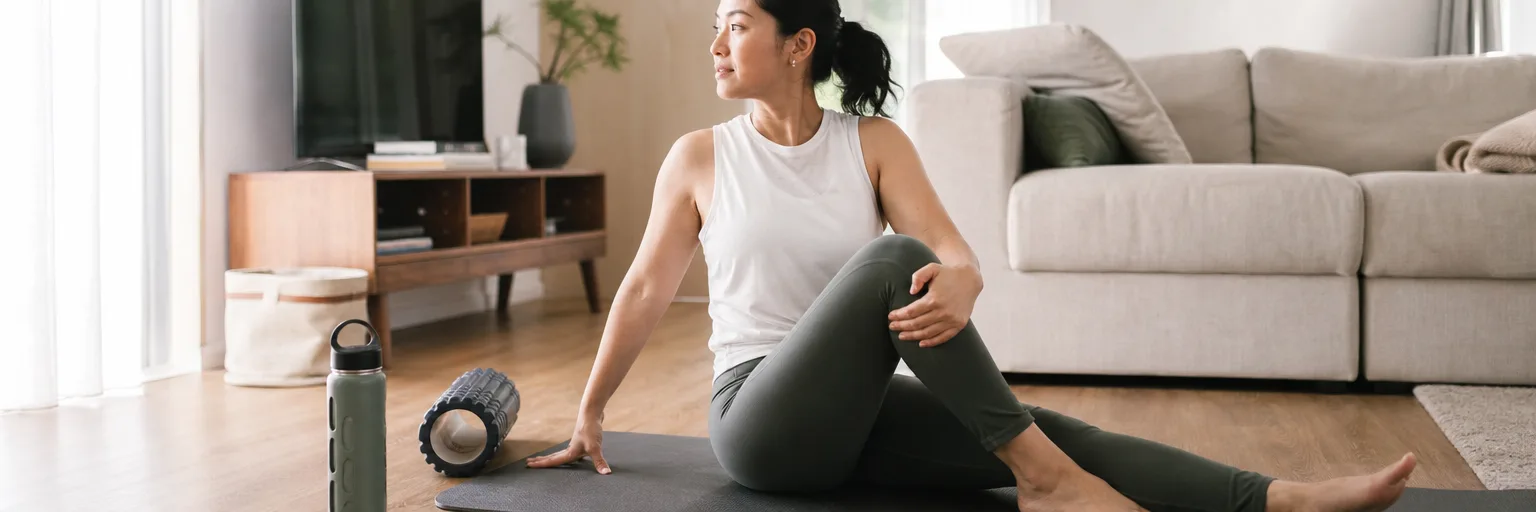 adult on a yoga mat doing a gentle seated stretch with a foam roller and water bottle as part of a fibromyalgia and weight-loss routine